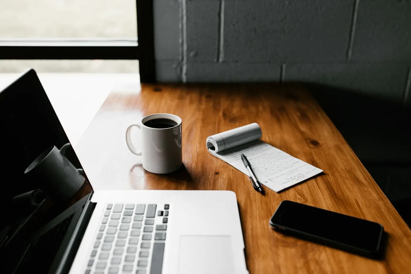 A laptop, a notebook and coffee on a wooden desk